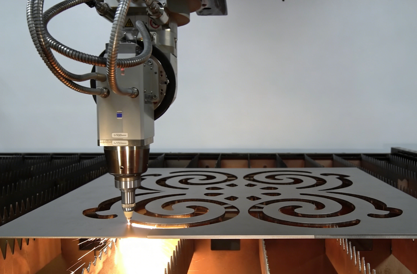 CNC laser cutting machine carving intricate decorative patterns into a metal sheet with sparks.