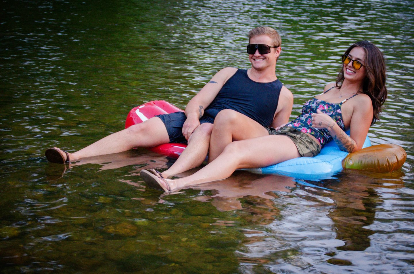 Two people sitting on an inner tube in the lake, wearing protective sunglasses