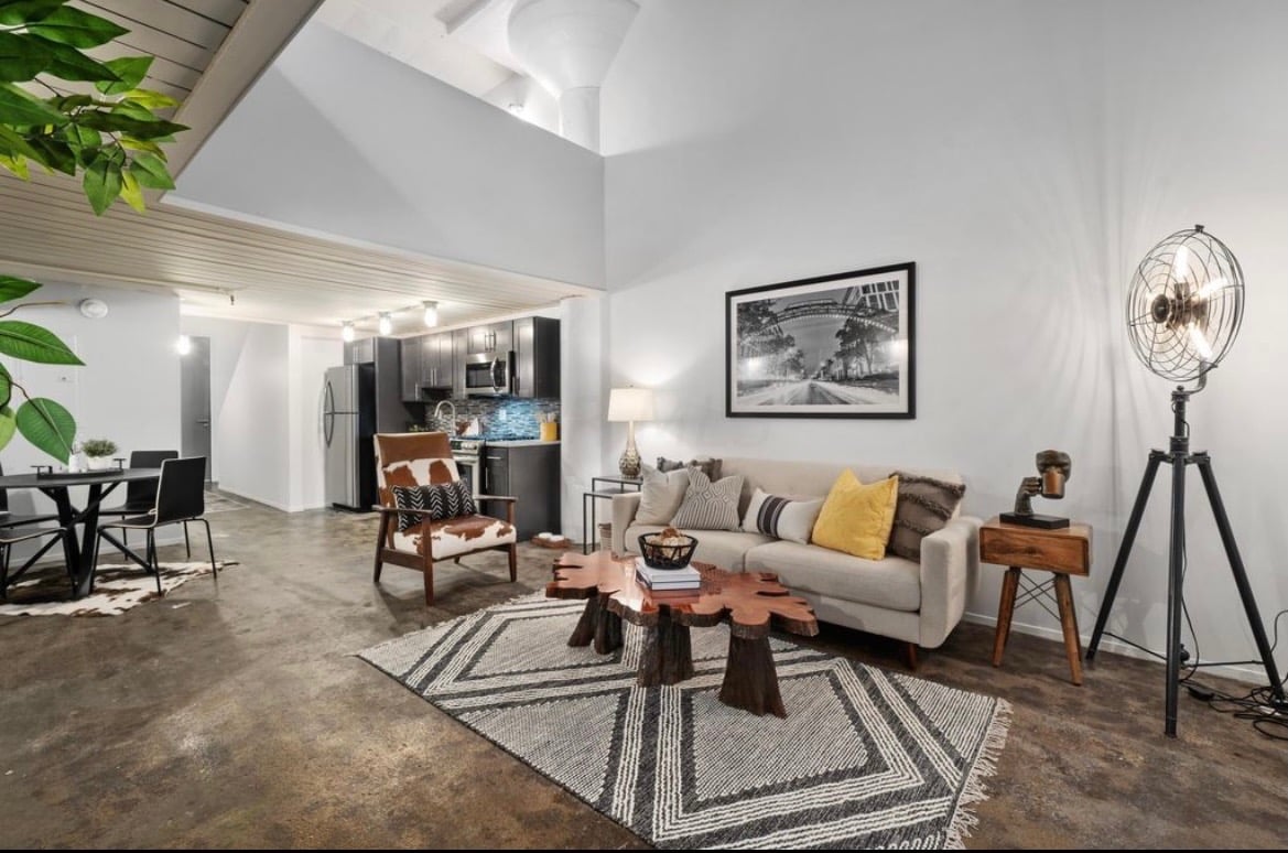 Modern industrial loft living room with live edge coffee table, beige sofa, and tripod floor lamp.