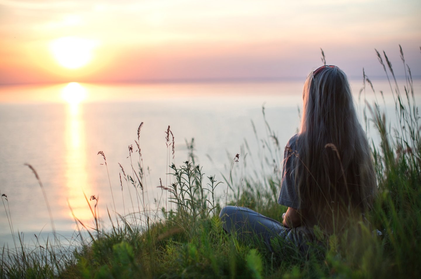 une femme assise dans l'herbe médite face à la mer pour être moins stressée