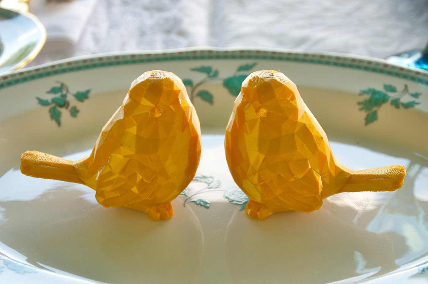 two golden bird ornaments sitting on a plate as wedding decoration