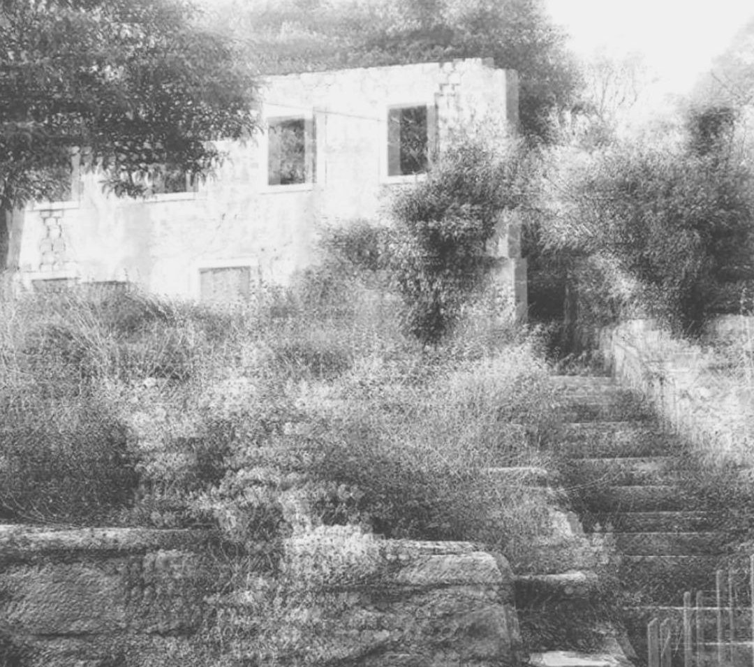 Black and white photograph of an abandoned stone house and overgrown stairs, used as a research header by artist Tina Bikic.