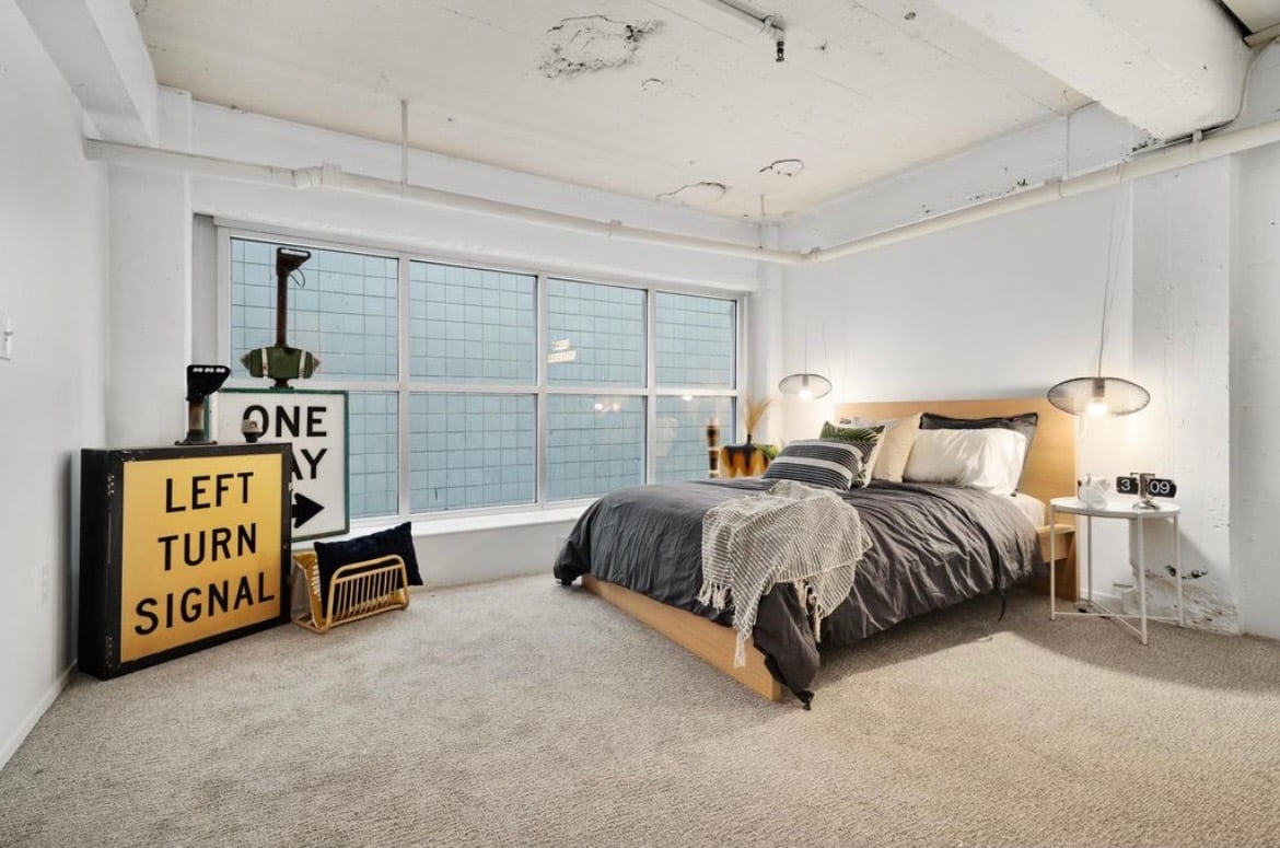 Modern industrial loft bedroom featuring a wooden bed, grey bedding, and vintage road signs.