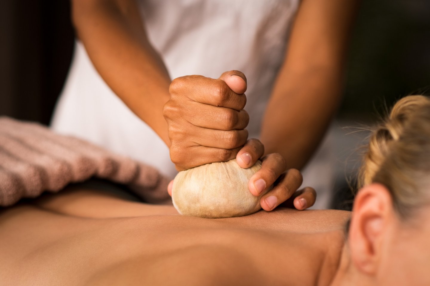 Professional massage therapist performing a herbal compress massage on a woman's back in a spa.