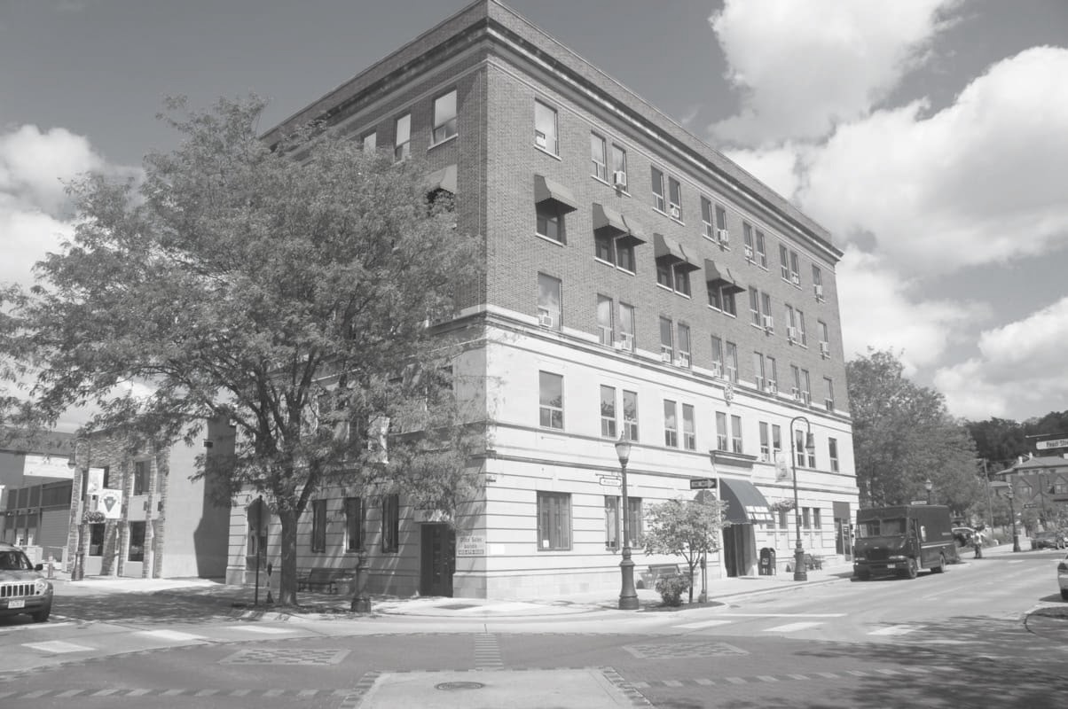 A black and white photo of a historic multi-story brick building on a city street corner.