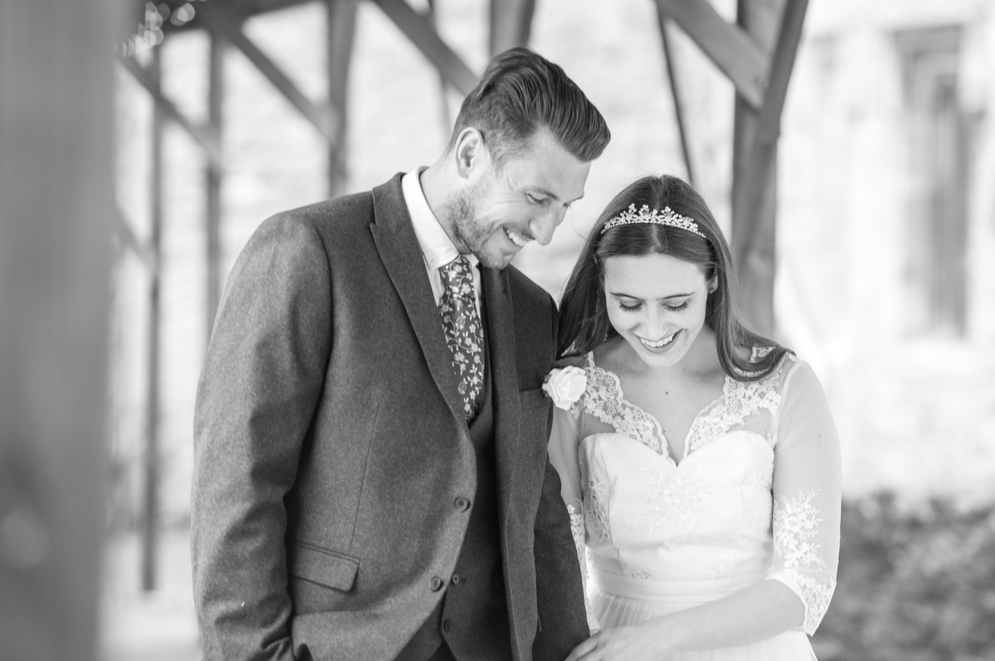 zoomed in black and white photo of bride and groom walking both laughing and smiling, archway framing them