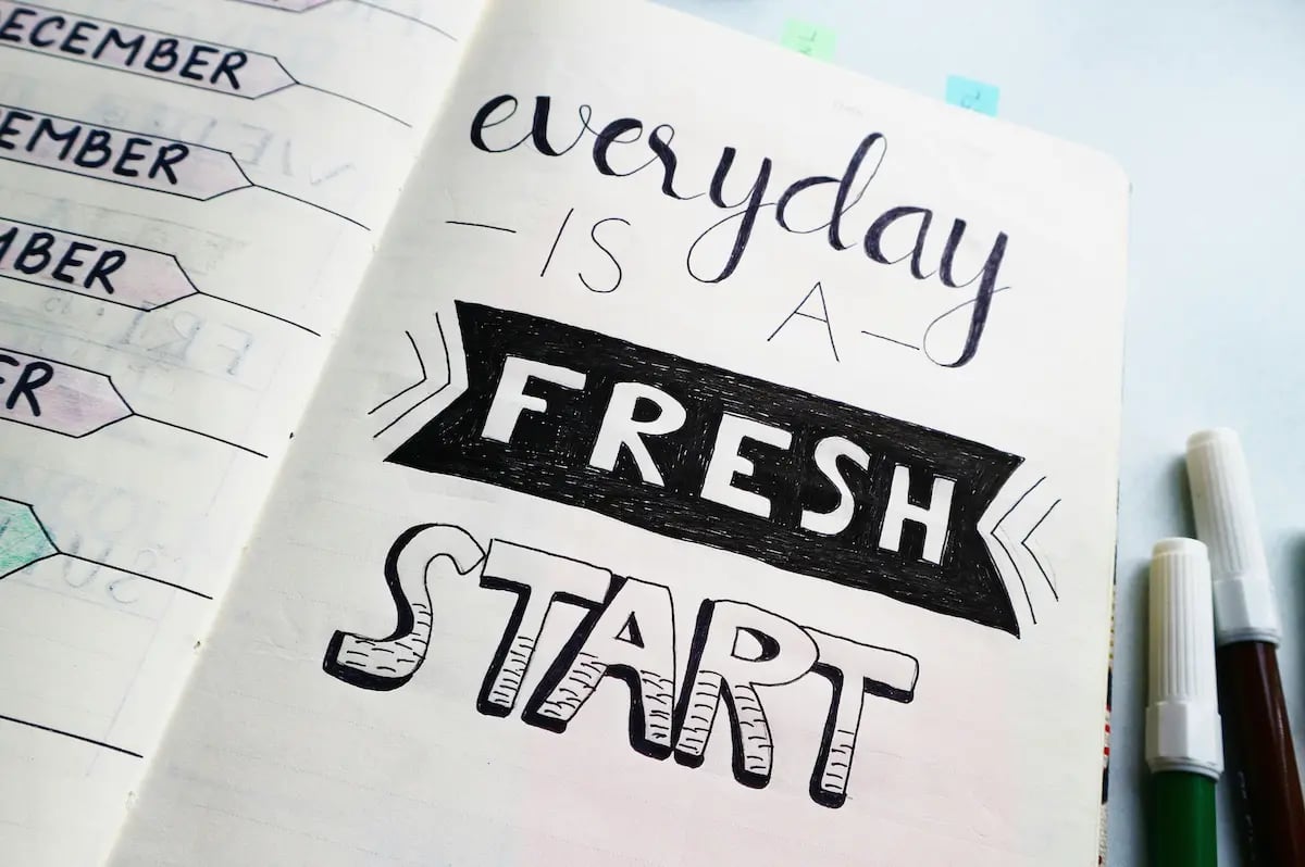 Hand-lettered motivational quote in a bullet journal says everyday is a fresh start with markers nearby.