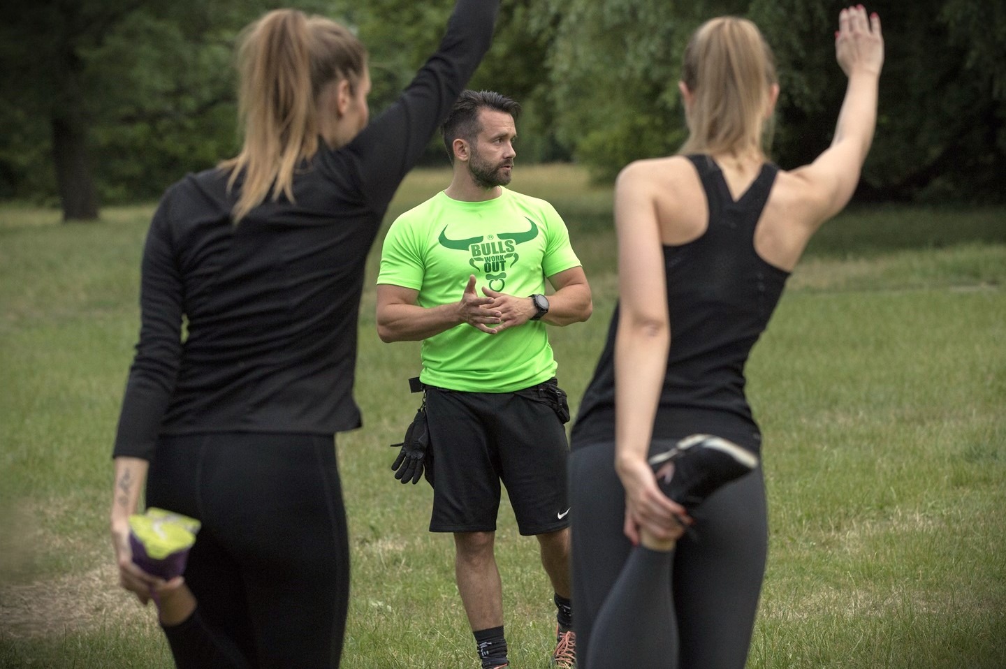 Trener stojący przed dwiema dziewczynami uprawiającymi stretching.
