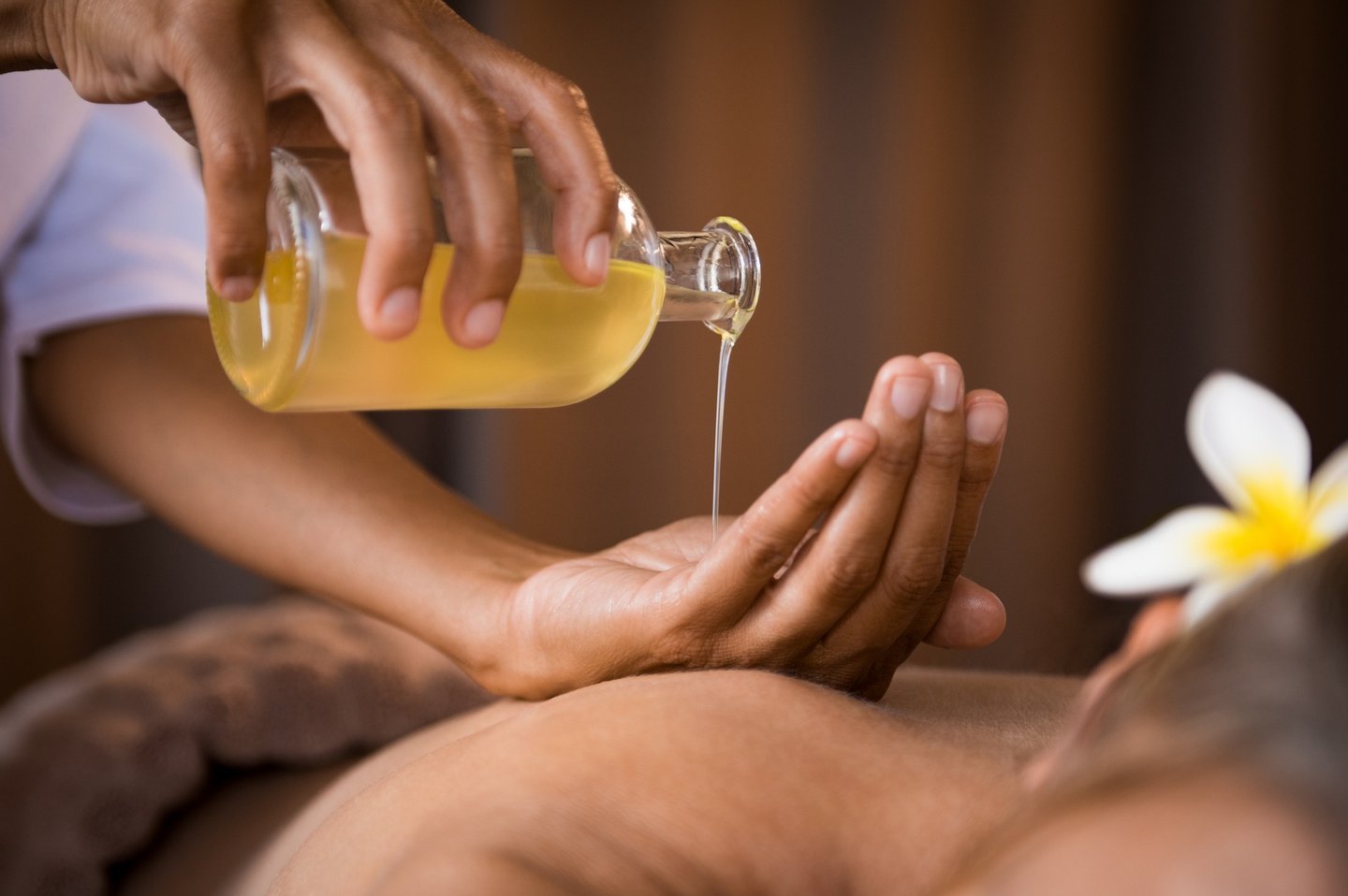 Therapist pouring essential massage oil onto hands for a relaxing spa body treatment.