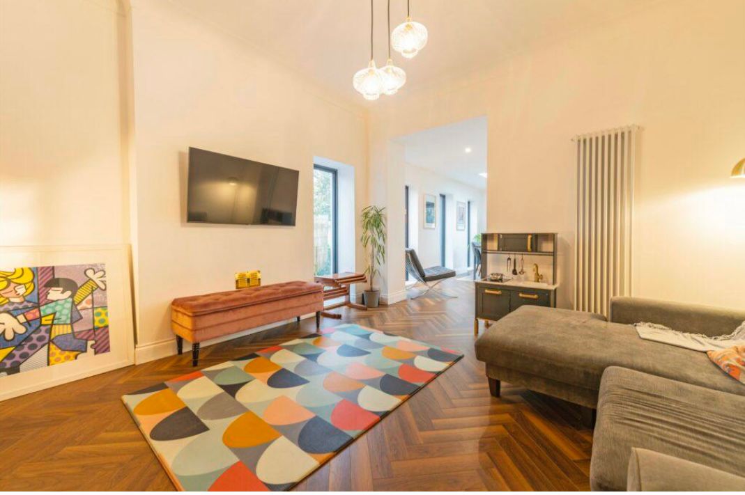 Modern living room featuring a colorful geometric rug, chevron wood flooring, and a wall-mounted TV.
