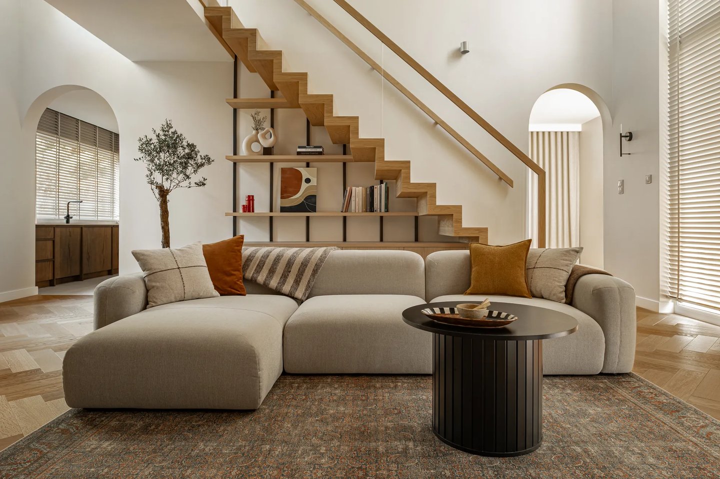 Fotografia wnętrz: przestronny salon ze schodami i dużym drzewkiem oliwnym.