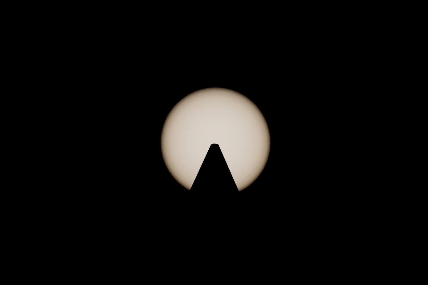 Symmetrical silhouette of an obelisk peak centered against a glowing sun, captured with a solar filter.
