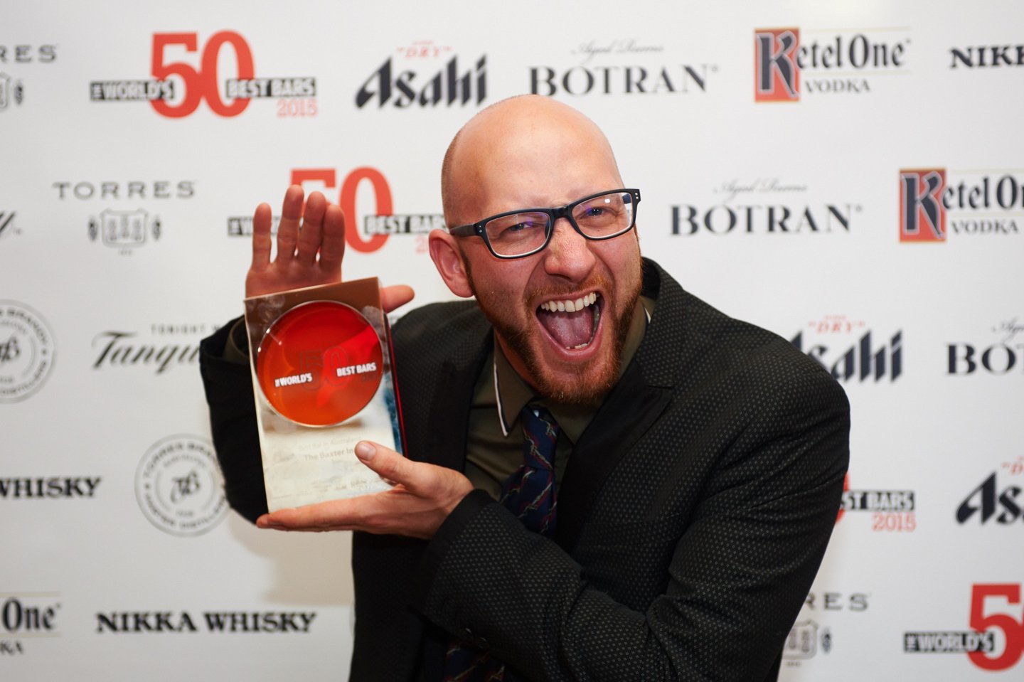 a man with a beard and glasses holding an award, he is very excited about winning