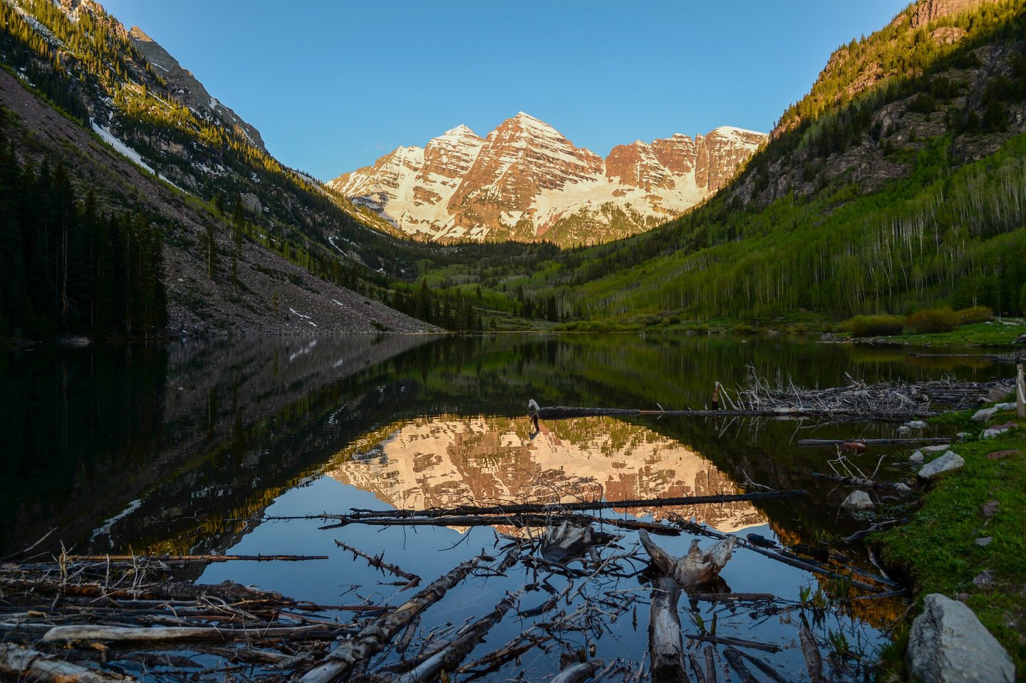 Spectacular Maroon Bells shine in the light of a summer sunrise with reflection in Maroon Lake