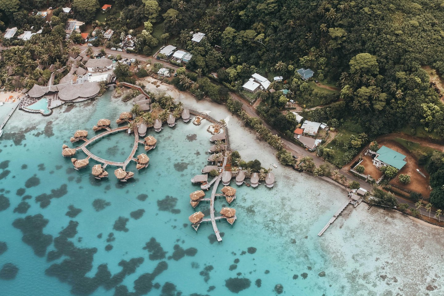 Aerial view of a tropical resort featuring overwater bungalows on clear turquoise water.