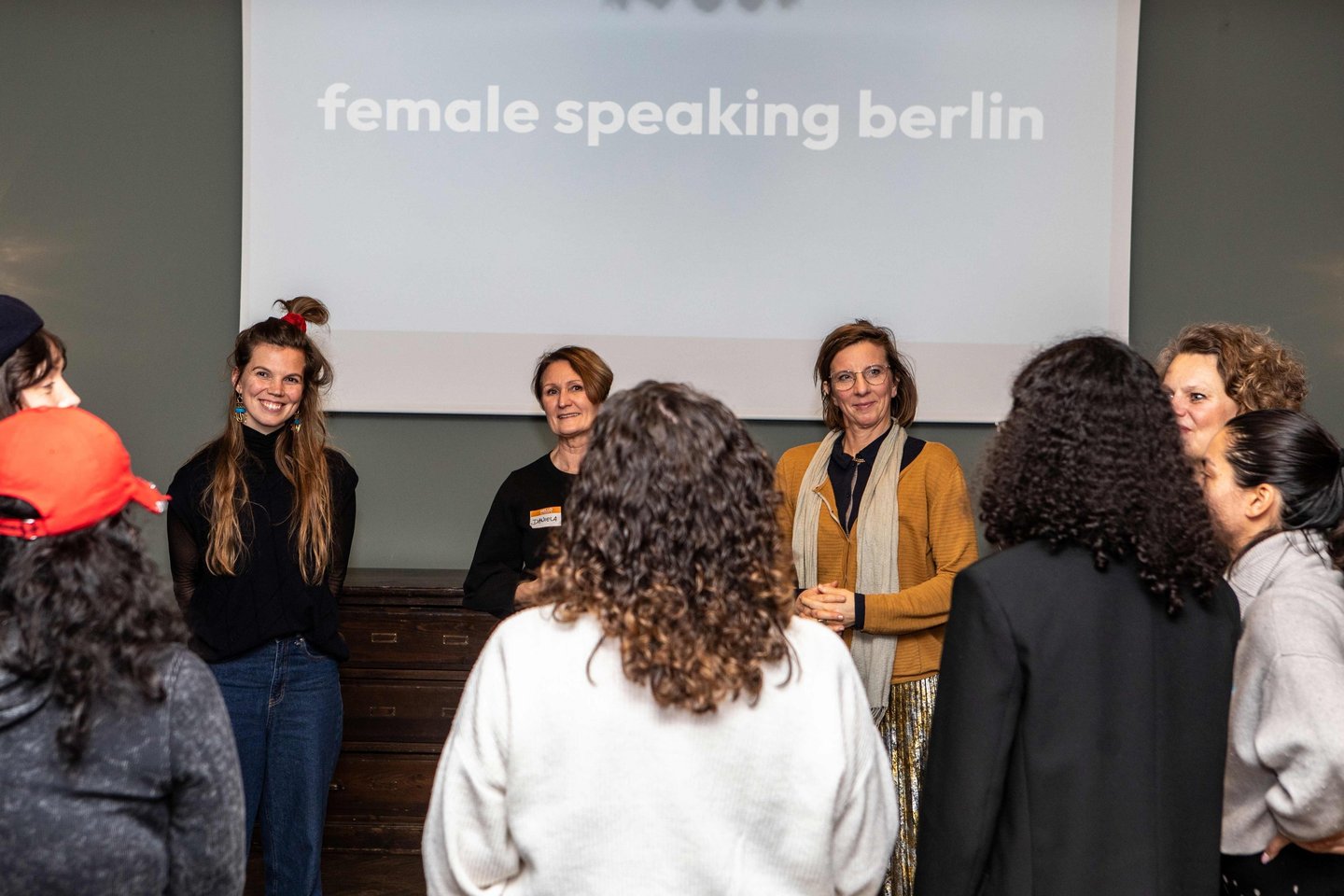 Women in circle, smiling and listening to each other, in workshop room, beamer logo female speaking