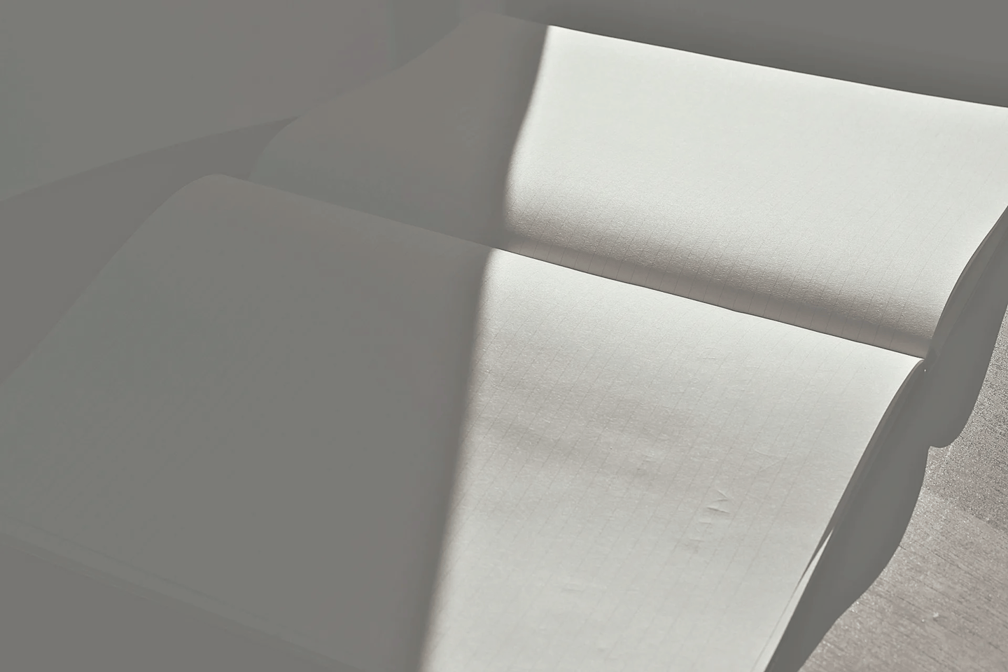 An open, lined notebook captured in a minimalist play of sharp sunlight and deep shadow.
