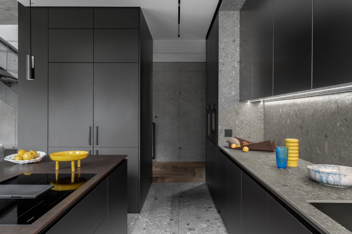 Nowoczesna ciemna kuchnia z wyspą, ściana i podłoga z szarego lastryko oraz żółte dodatki.