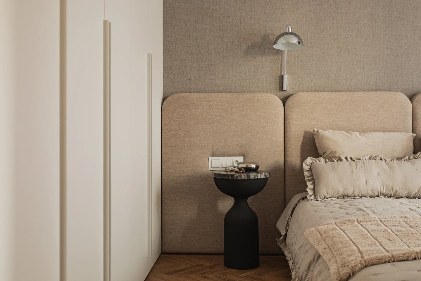 Fotografia wnętrz: biała szafa w sypialni, czarny stolik nocny i tapicerowane panele ścienne.