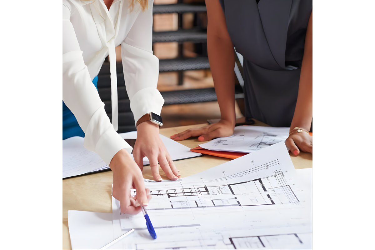 Two female architects reviewing floor plan blueprints on a desk for a building project.