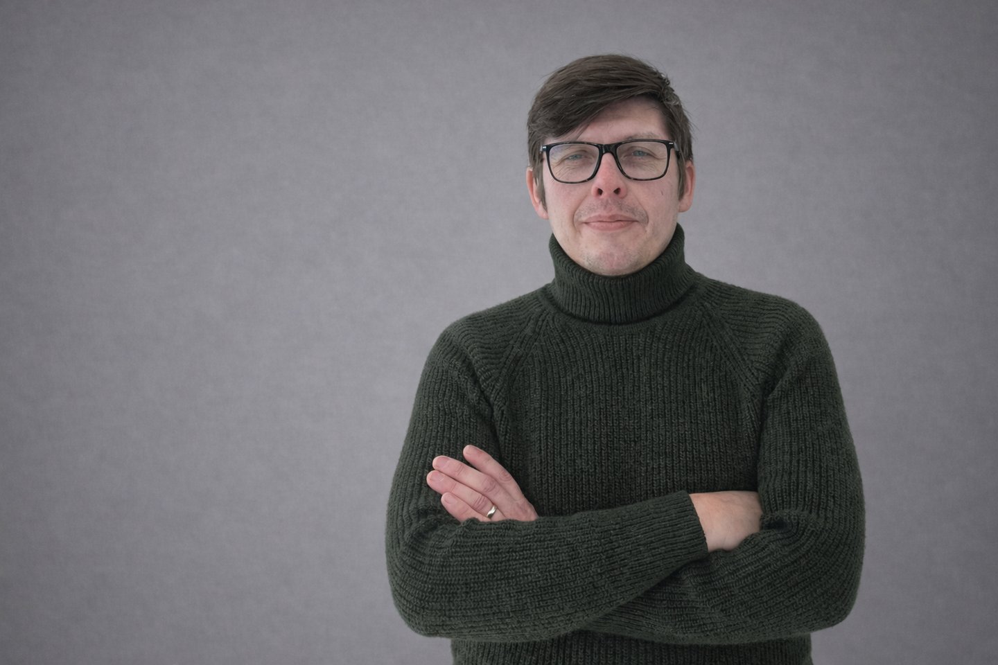 Professional portrait of a man wearing glasses and a dark green turtleneck sweater.