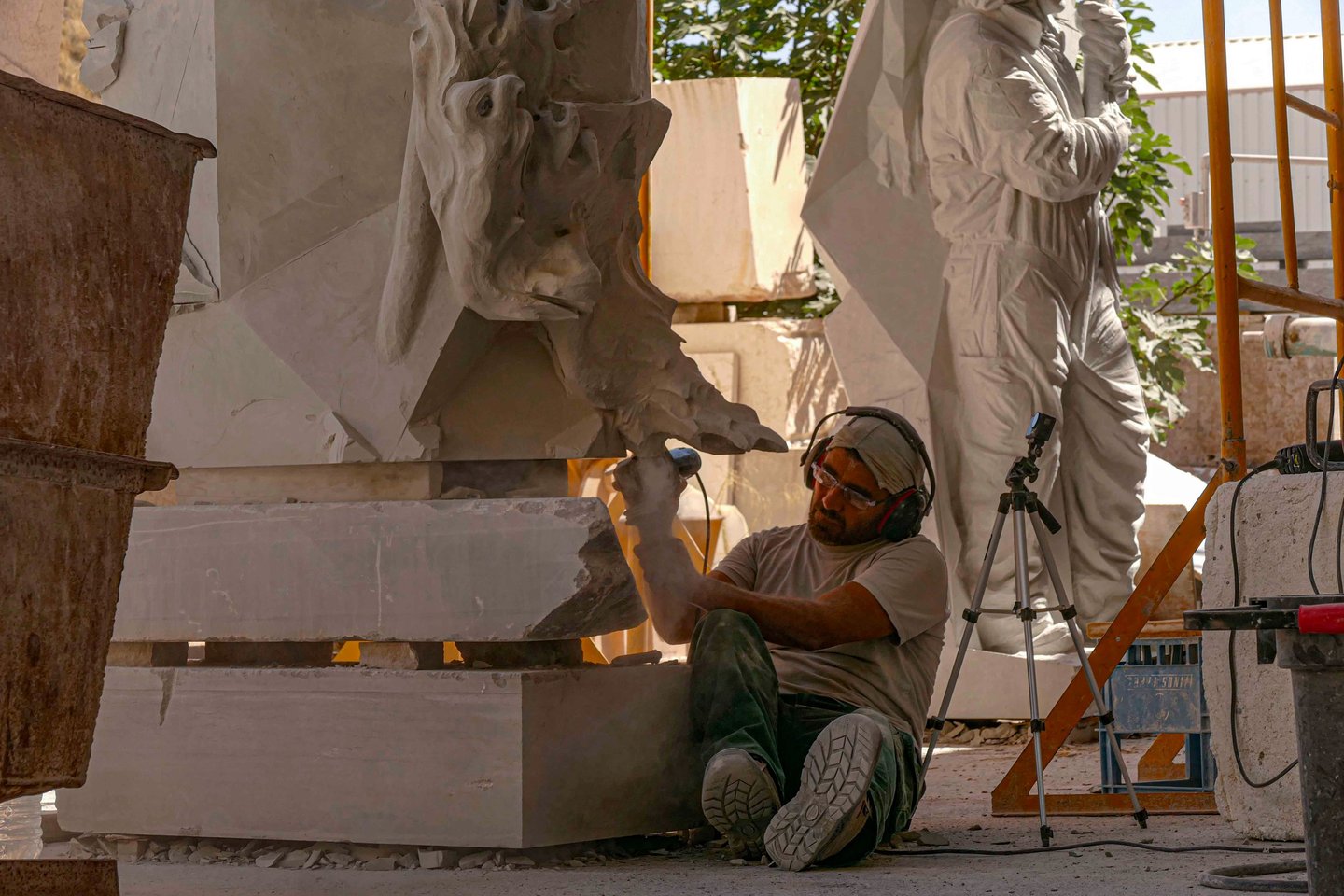 Professional sculptor using a power tool to carve intricate details into a large sandstone statue.
