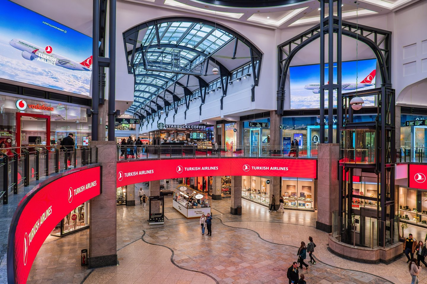Modern shopping mall interior with glass elevators, Starbucks, and Turkish Airlines advertisements.