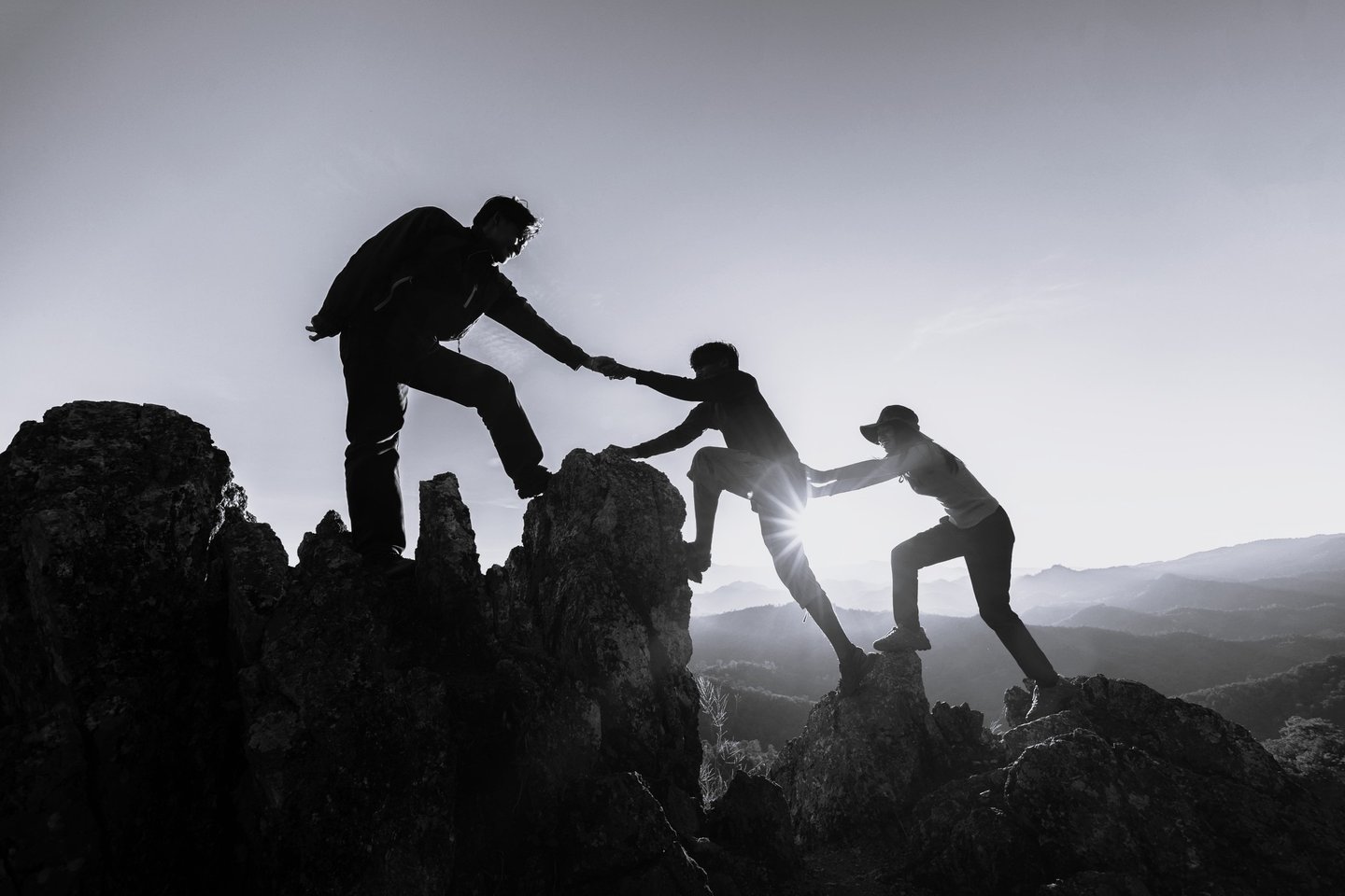 a group of people helping each other to climb up to the top of a mountain