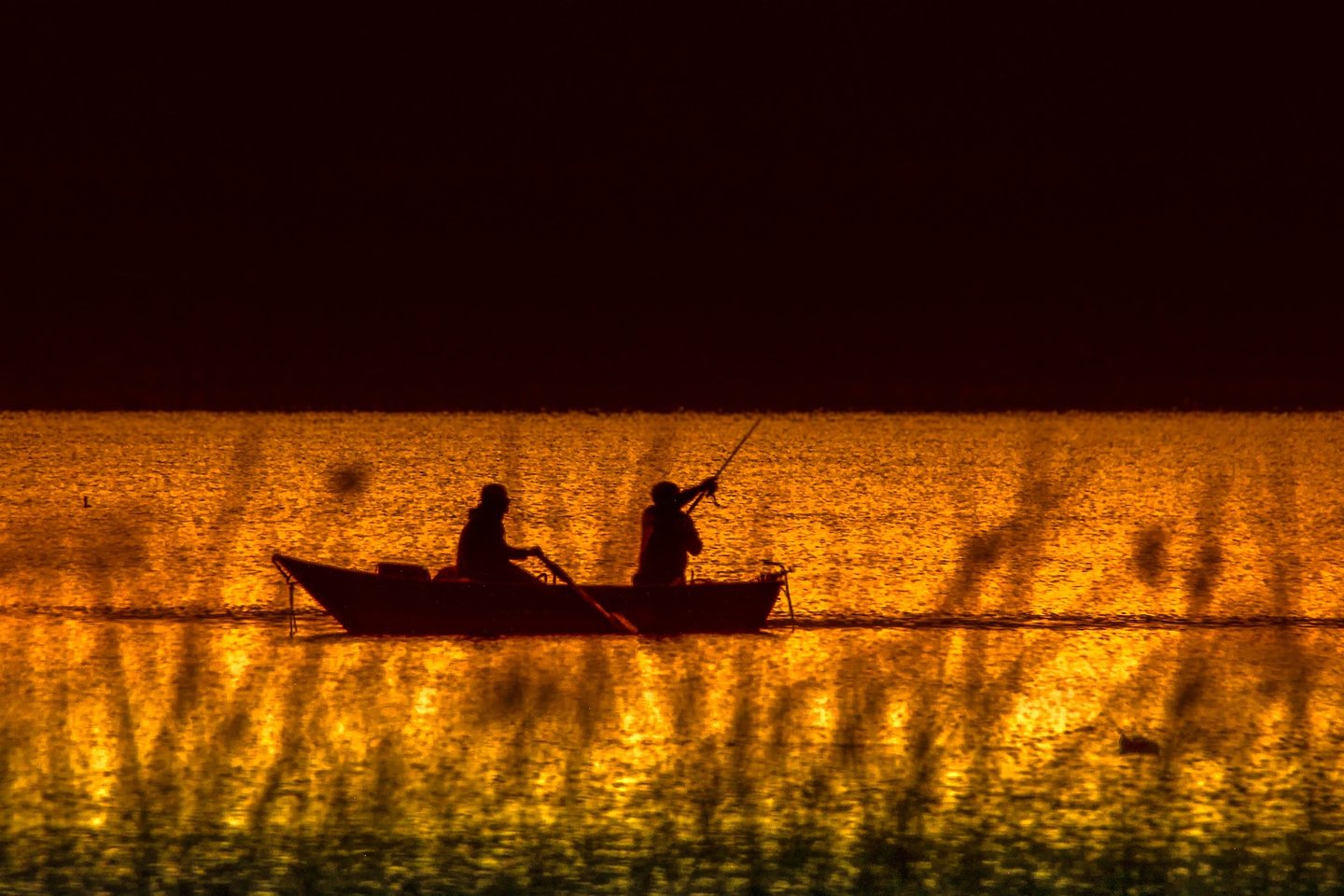 two people fishing in a lake at sunset