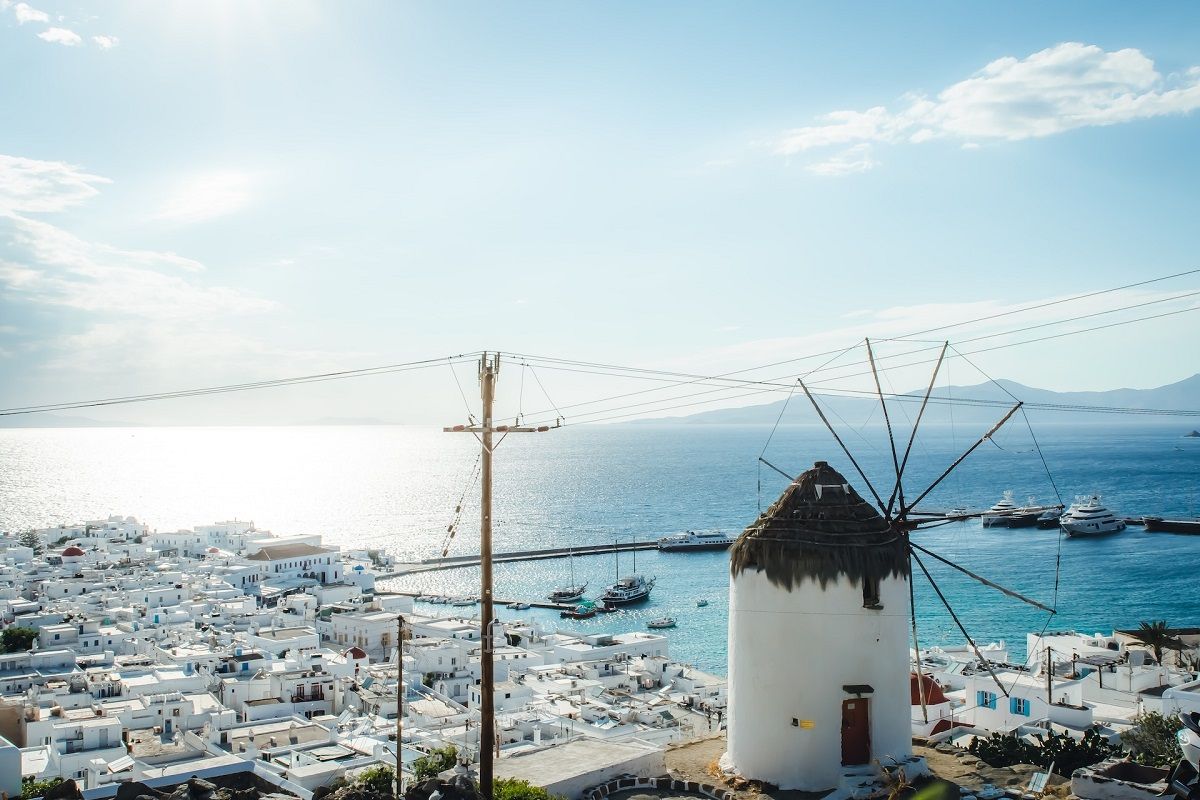 Panoramic view of a traditional white Mykonos windmill overlooking white houses and the Aegean Sea.