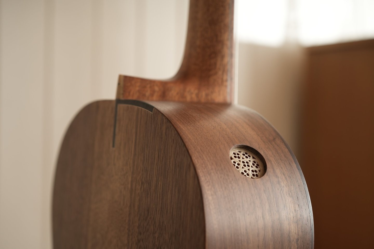 Close-up of a handcrafted acoustic guitar with a walnut body and a unique side sound port.