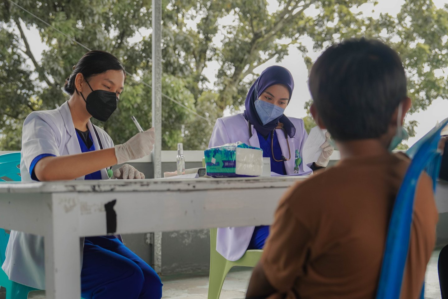 Dokter wanita berjilbab dan bermasker memberikan konsultasi kesehatan kepada anak di area terbuka