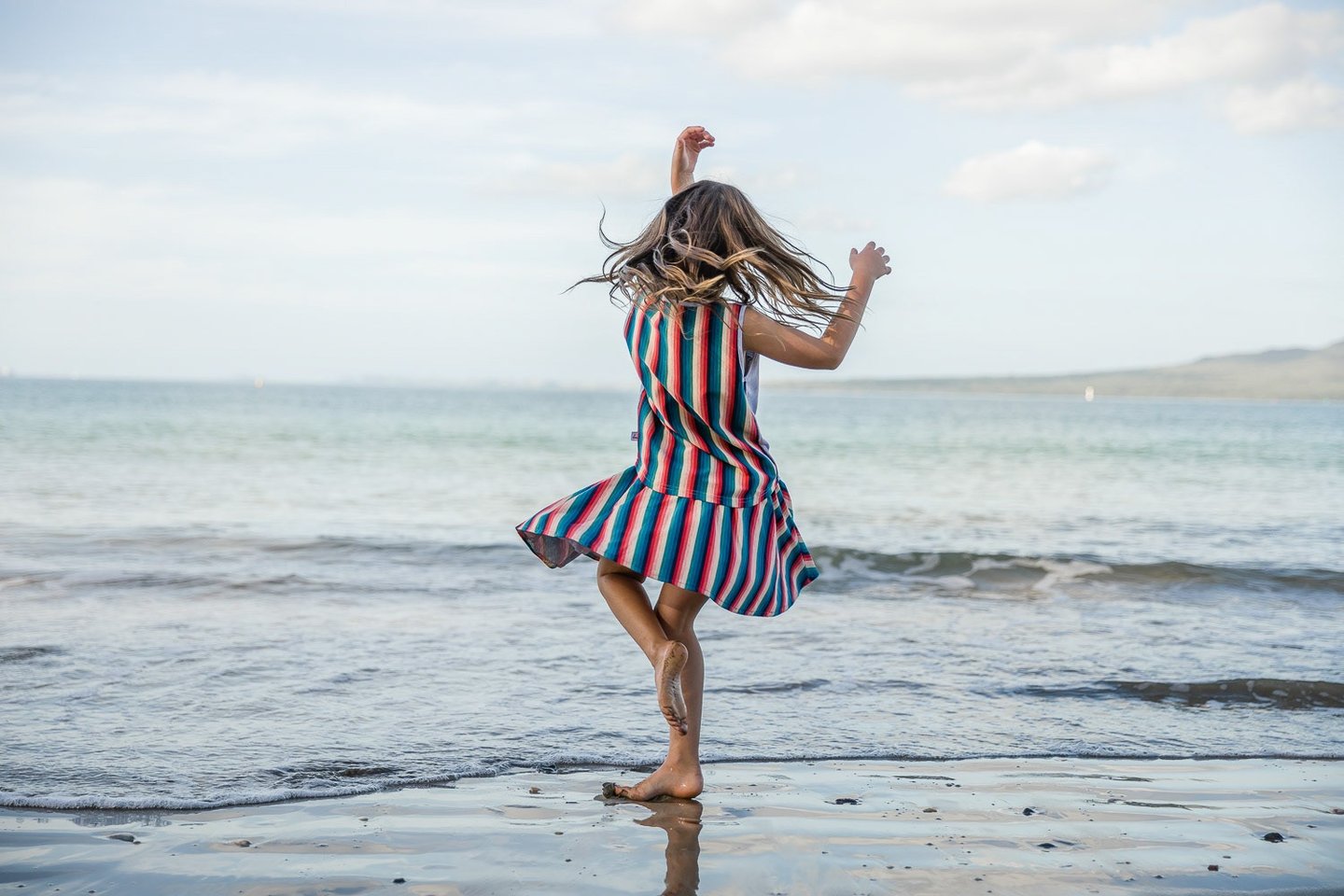 Fashion photography - a girl in a striped dress dancing on the beach
