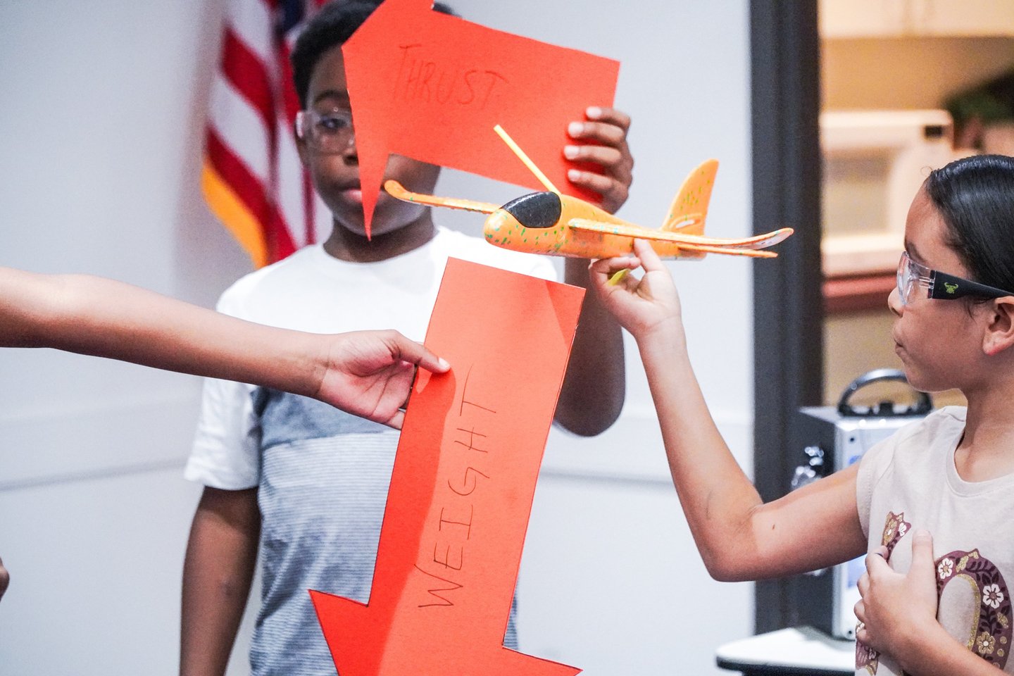 a young girl is holding a glider while other children hold force vectors lift drag thrust and weight