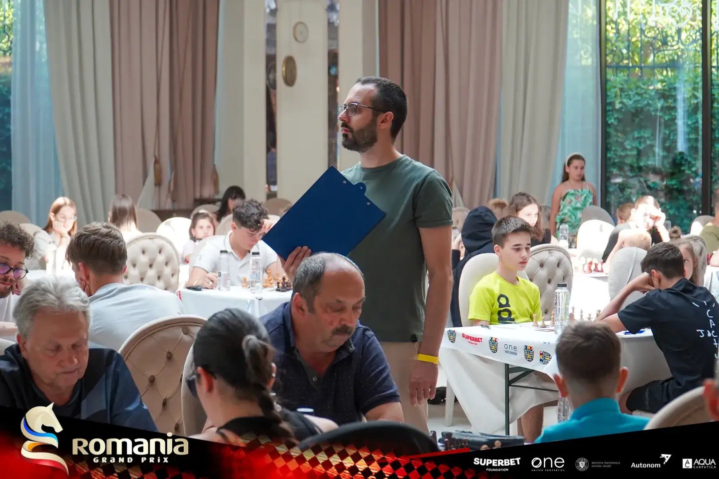FIDE Arbiter Vlad Ghita holding a clipboard in the middle of a tournament hall and watching games