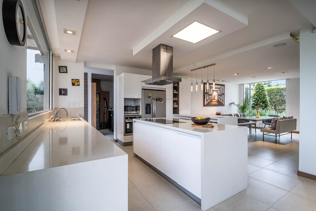 Vista lateral de una cocina estilo americano, paredes blancas y comedor con amplios ventanales