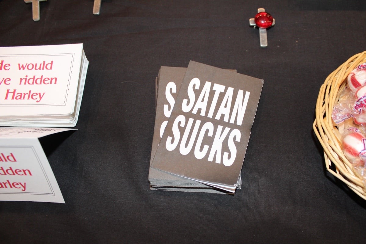 Free handouts at biker ministry table says “Satan Sucks.”