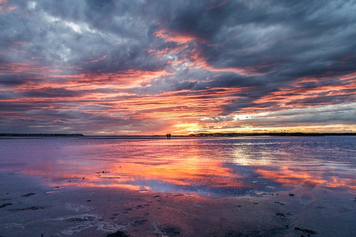 Vibrant pink and purple sunset over a beach with dramatic clouds reflecting on the wet sand.