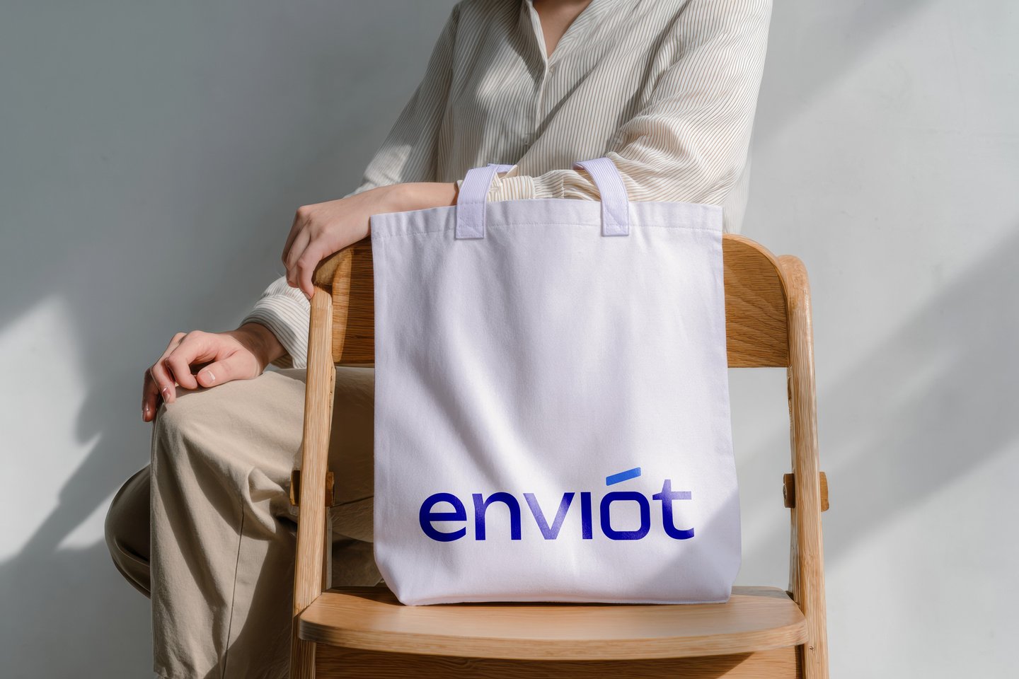 A person sitting on a wooden chair with a white Enviót branded canvas tote bag.