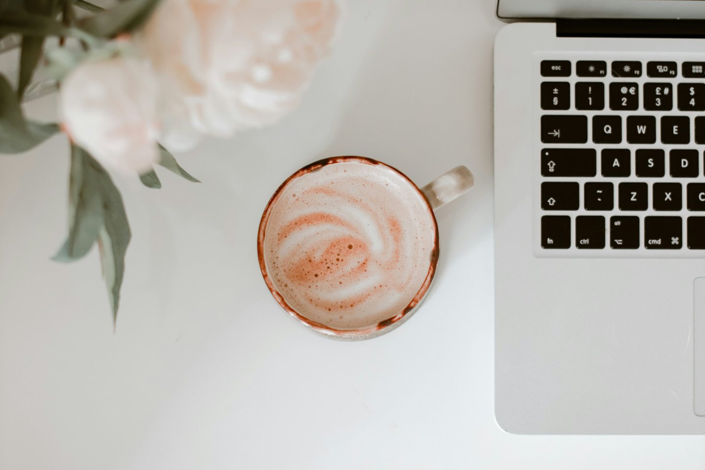 un espace bureau appaisant pourvu d'une tasse de café, des fleurs roses pales et un clavier d'ordinateur