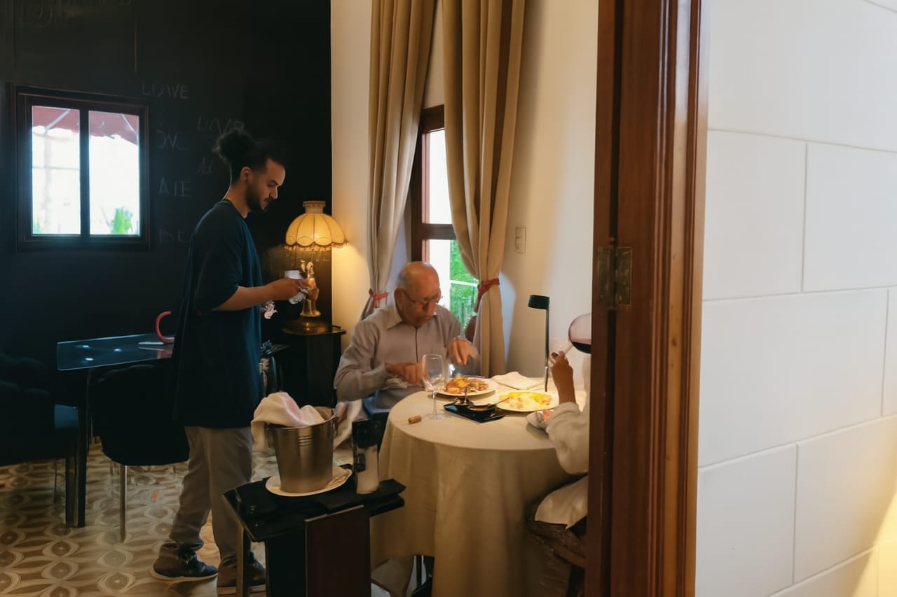 A professional waiter serving an elderly couple dining at a fine dining restaurant table.