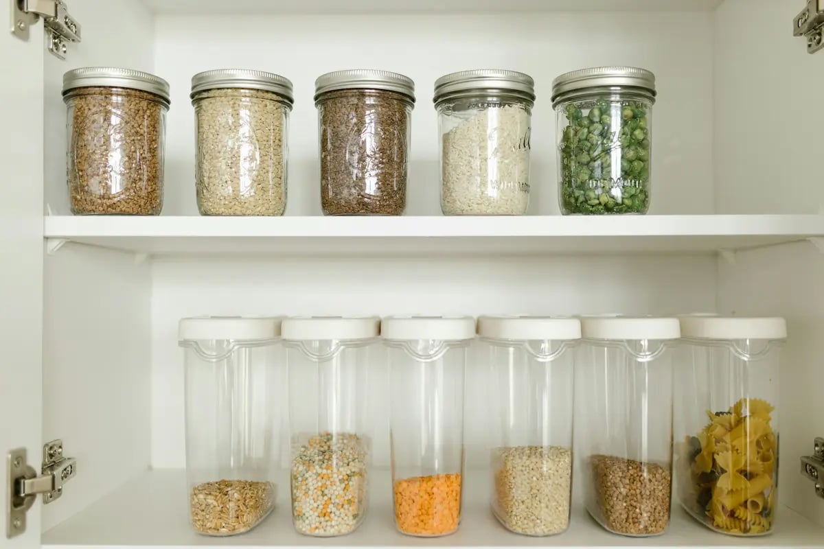 Organized kitchen pantry featuring glass mason jars and clear airtight containers filled with bulk dry goods.