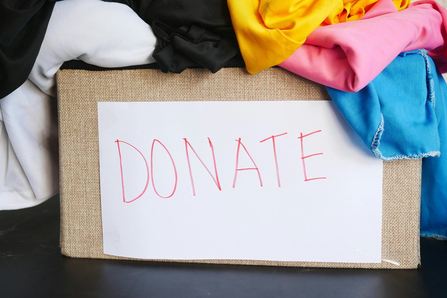 A cardboard box filled with colourful clothes for donation featuring a handwritten donate sign.