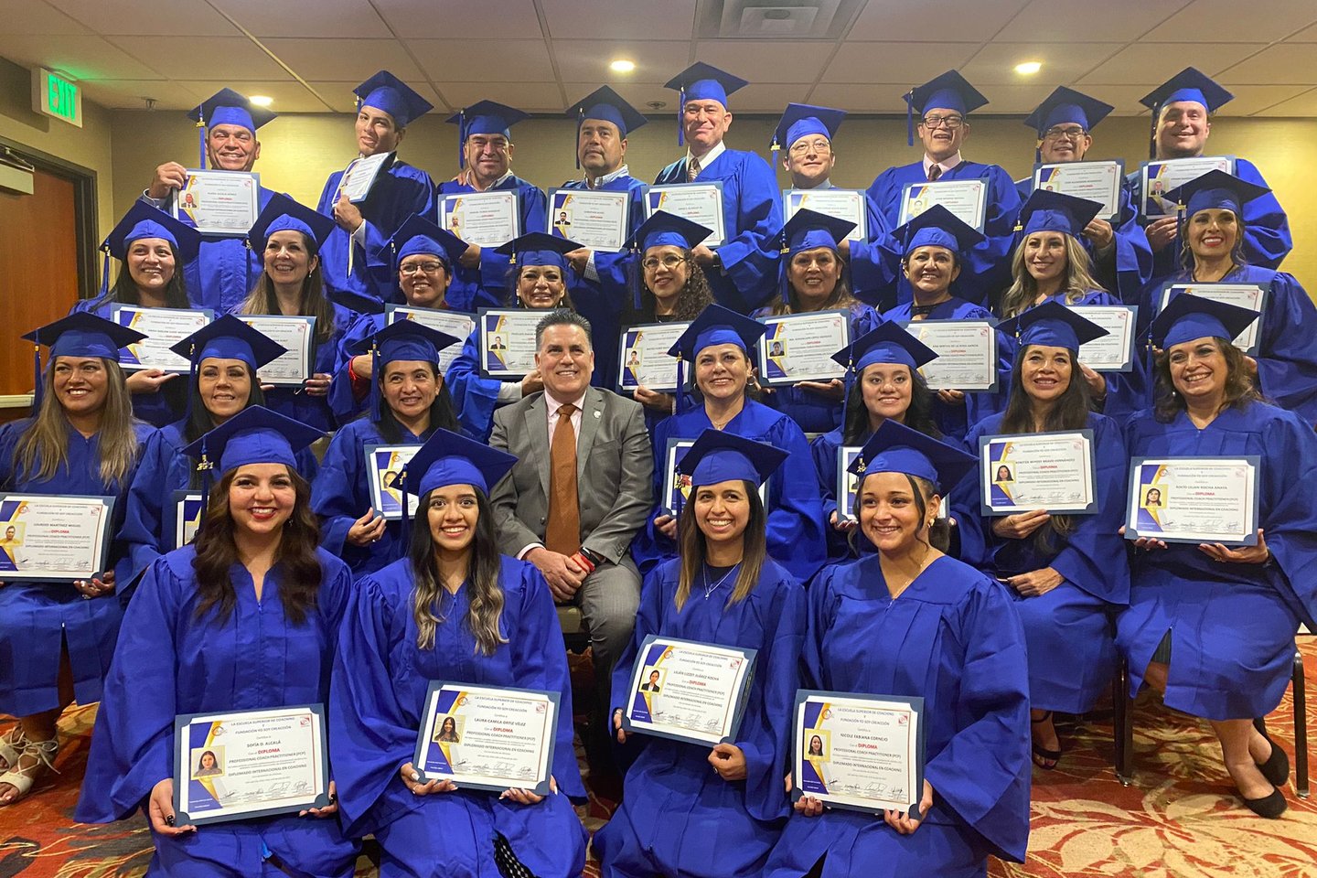 A diverse group of graduates in blue caps and gowns holding diplomas at a graduation ceremony.