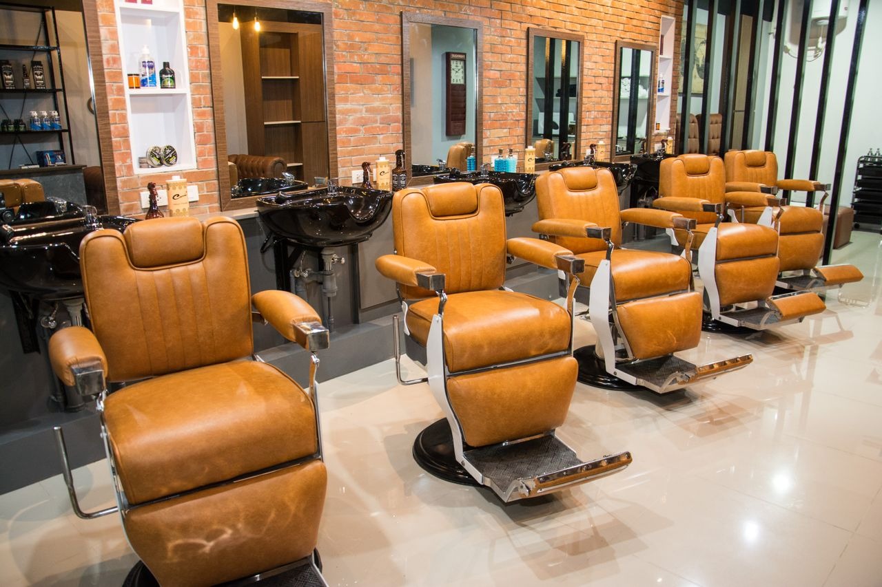 Modern salon interior featuring tan leather styling chairs and brick walls.