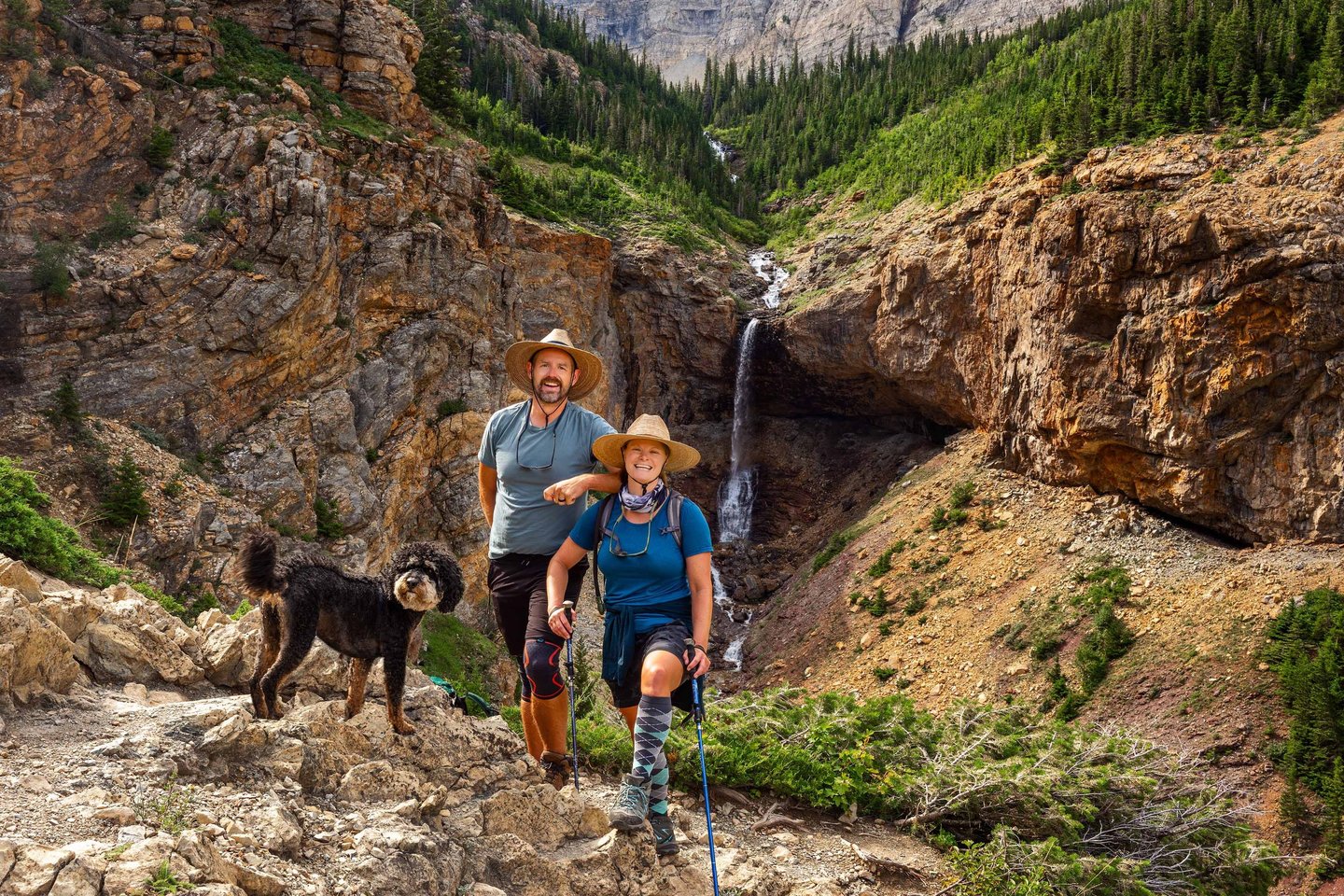 Hikers with dog on the Crypt Lake Trail beside a waterfall in Waterton Lakes National Park.