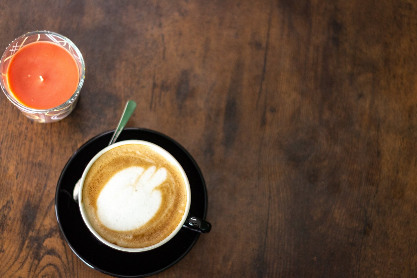 Hot cappuccino with latte art and a lit candle on a rustic wooden table.