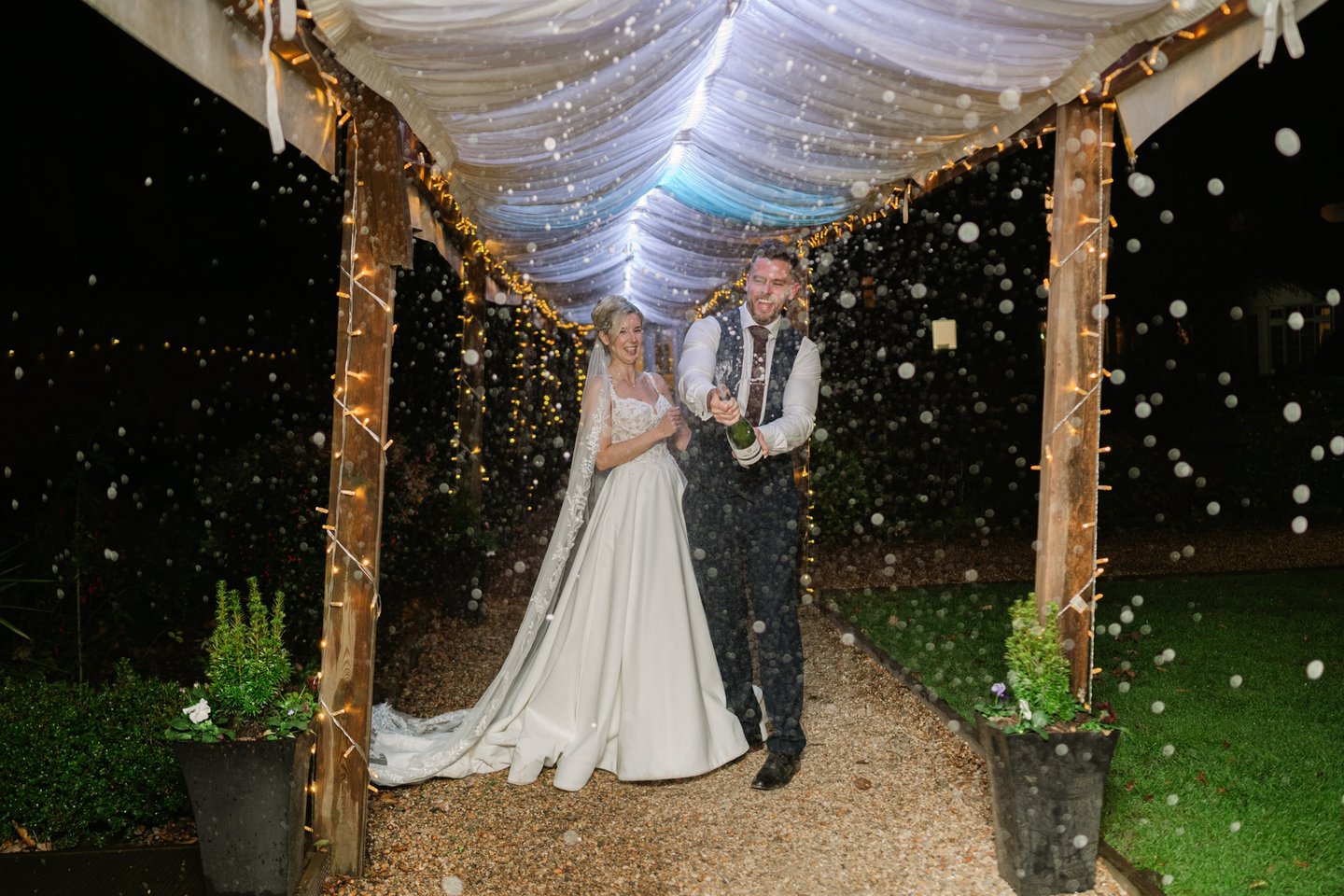 Couple spraying champagne under a pergola at The Mill House Hotel during their wedding