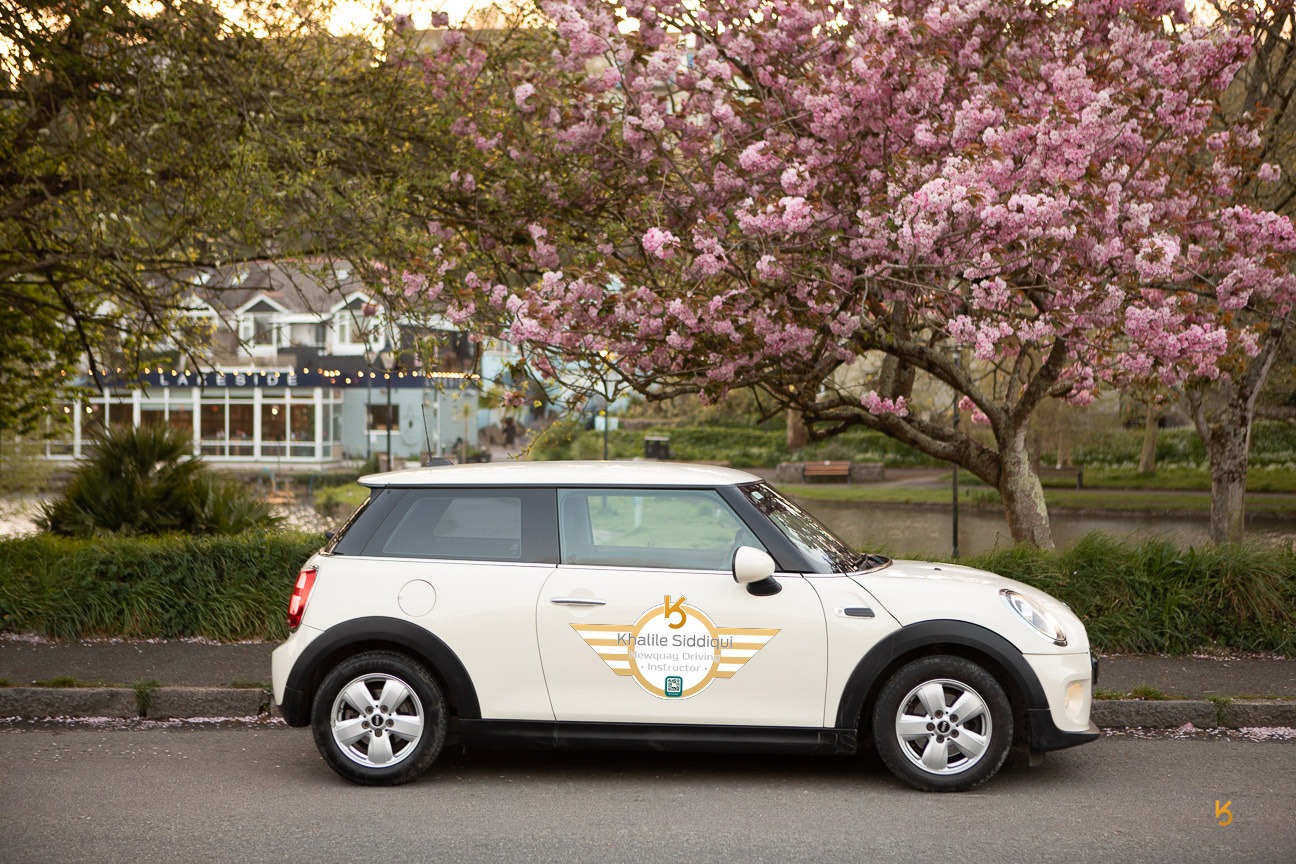 White Mini Cooper driving instructor car parked by pink cherry blossom trees in Newquay.