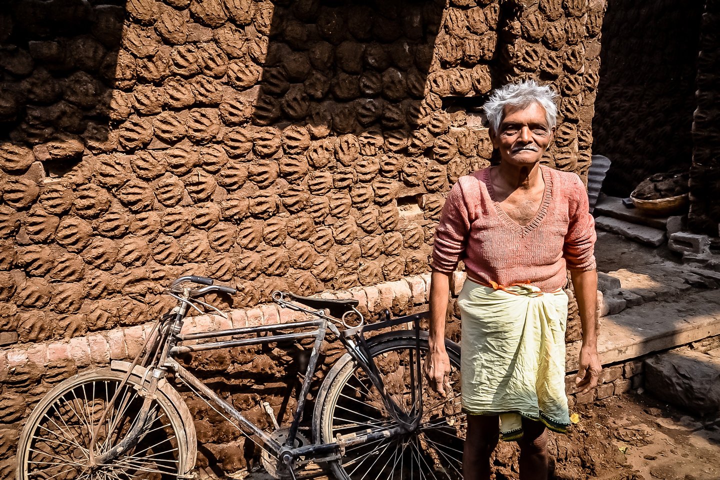 Showing his work of cow dung paddies for fuel drying in the sun against a wall in Varanasi, India.